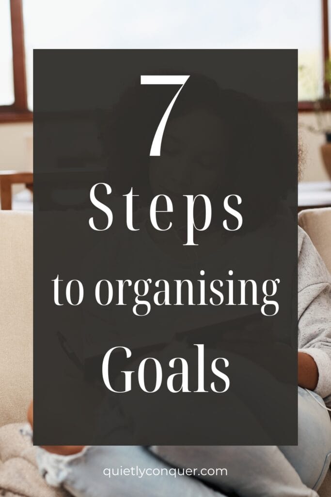 Text reads - 7 steps to organising goals. WOman sat on sofa with a book in hand.