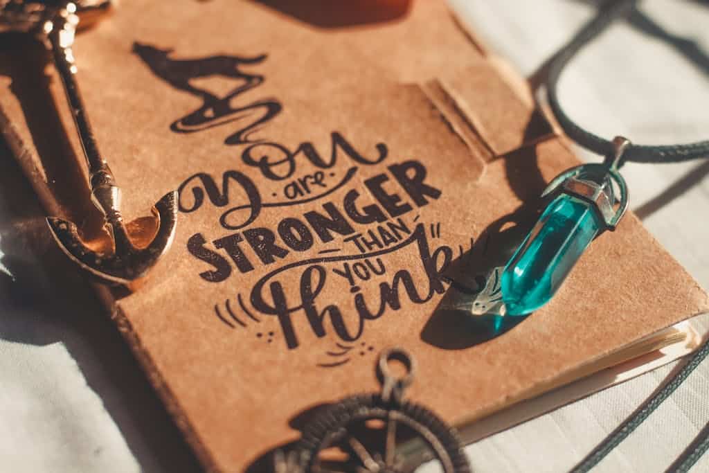 Brown booklet with inspiring text and necklace, featuring a blue crystal pendant in warm daylight.