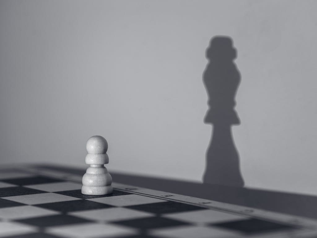White chess pawn casting a shadow of a queen, symbolizing growth and transformation.