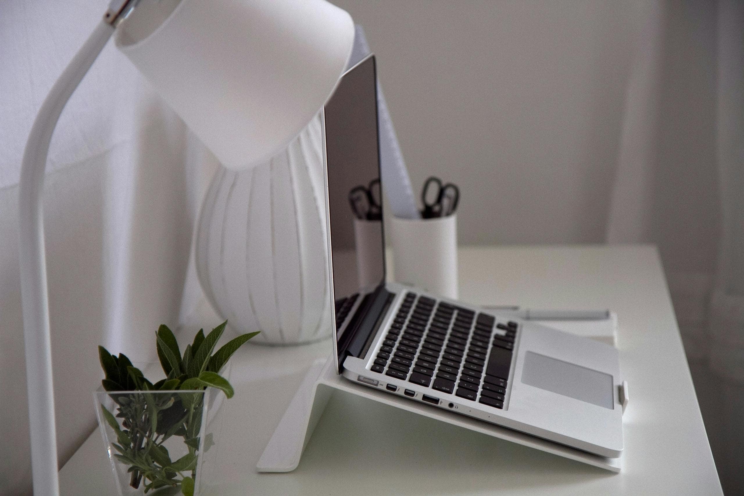 Modern home office with a laptop, desk lamp, and plant on a white desk.