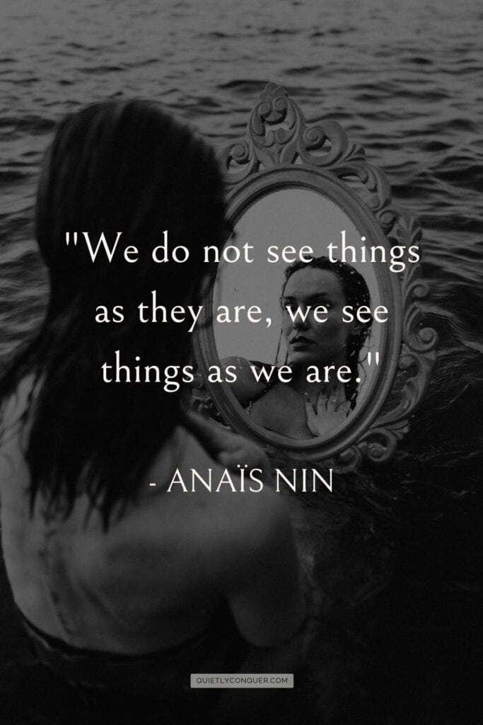Black and white images of a Woman looking in mirror sat on sand. Quote reads "We do not see things as they are, we see things as we are" Anaïs Nin