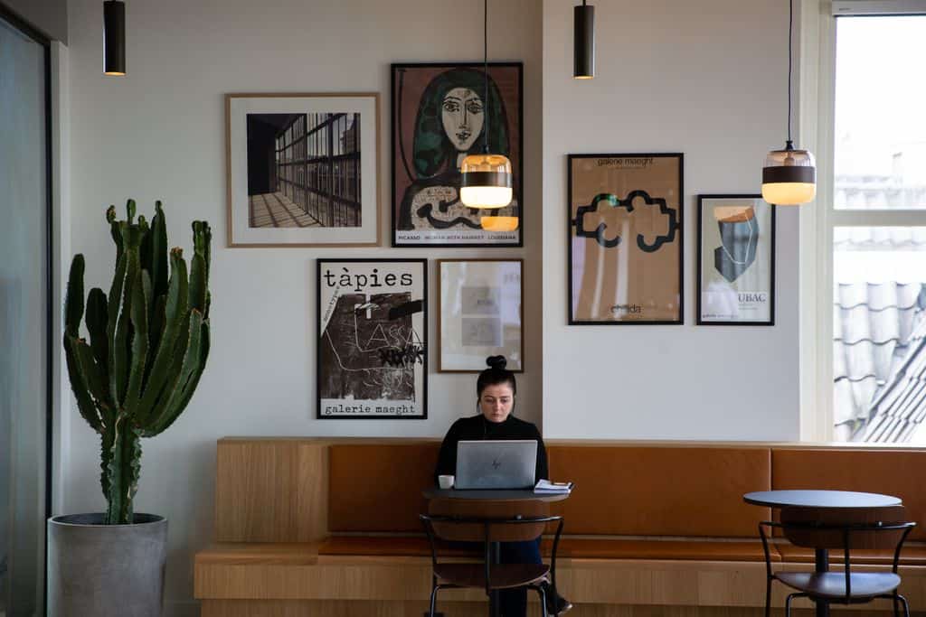 Introvert Coach in Business. Image shows a woman working on a laptop in an Amsterdam café, surrounded by eclectic art and modern lighting.